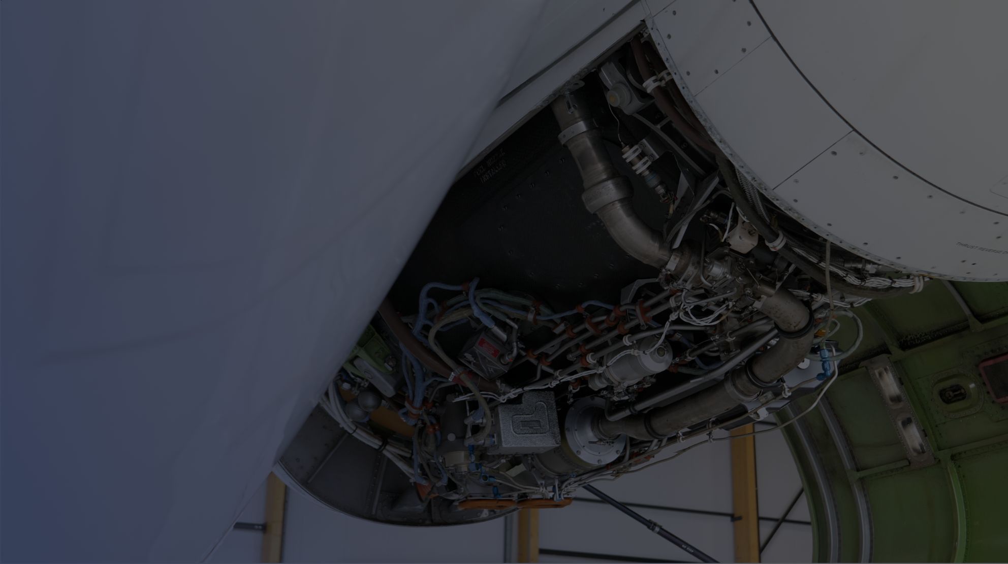 Close-up view of an aircraft engine compartment showing various pipes, cables, and mechanical components.